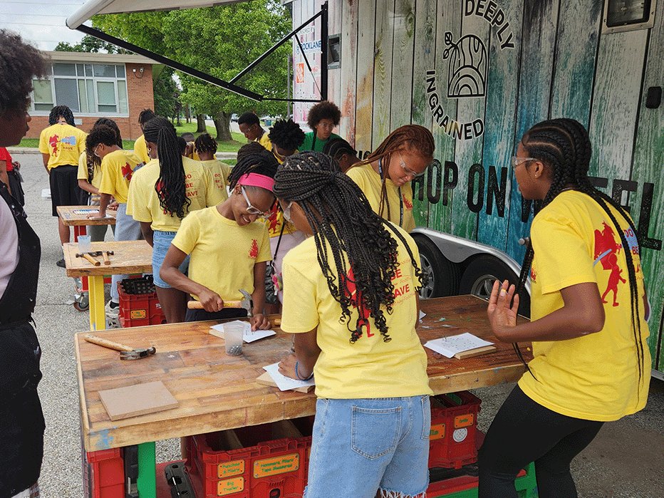 Campers in yellow shirts building at the Woodshop on Wheels trailer at St. Florian Center